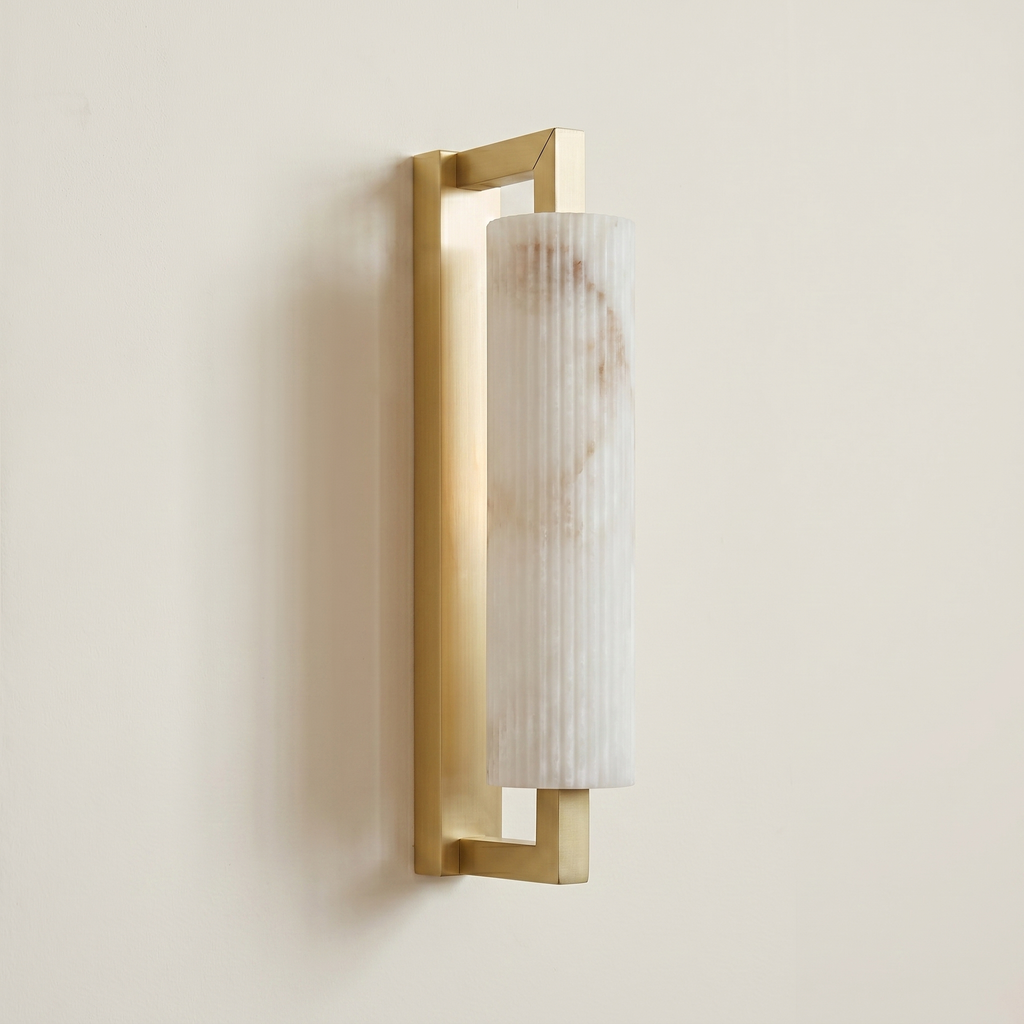 Pilaster Alabaster Cylinder light fixture with a tall, cylindrical alabaster shade and a brushed brass metal frame, shown illuminated against a plain off-white wall. | IINK Interiors
