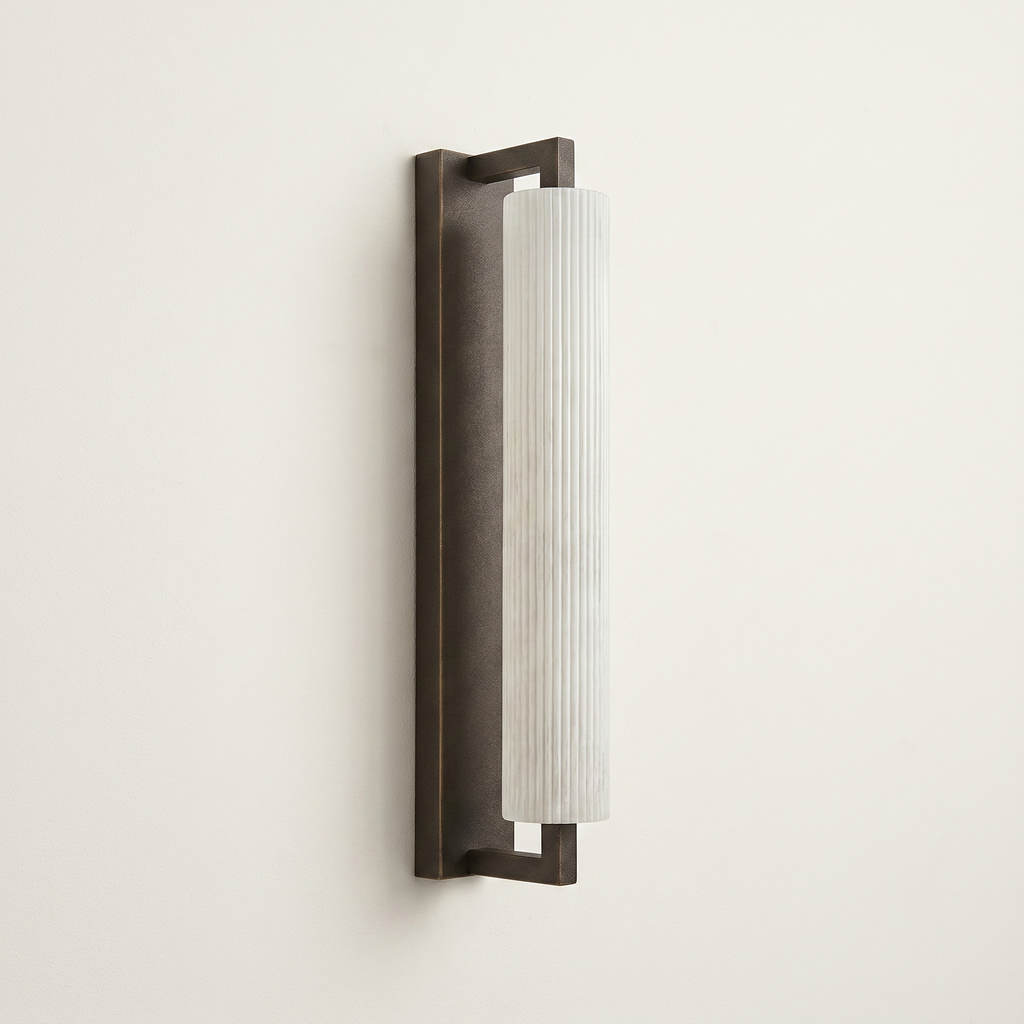 Pilaster Alabaster Cylinder light fixture with a tall, cylindrical alabaster shade and a brushed bronze metal frame, shown illuminated against a plain off-white wall. | IINK Interiors