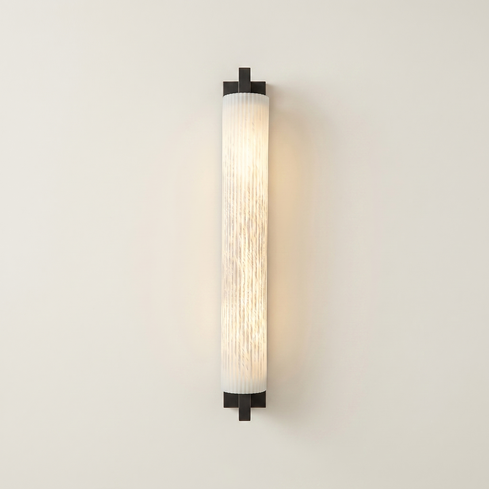 Pilaster Alabaster Cylinder light fixture with a tall, cylindrical alabaster shade and a brushed bronze metal frame, shown illuminated against a plain off-white wall. | IINK Interiors
