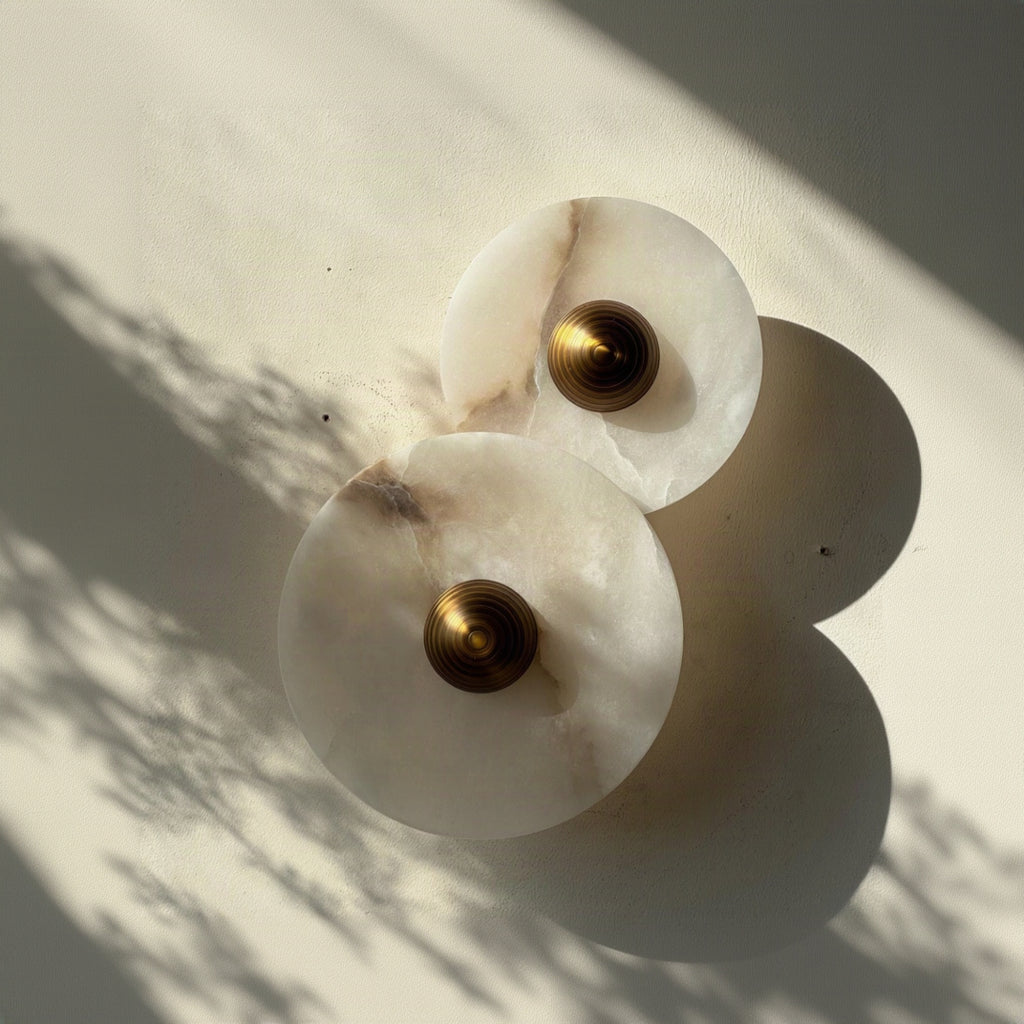 Two white Alabaster marble wall sconces with gold centers on a light background. IINK Interiors