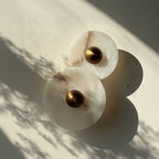 Two white Alabaster marble wall sconces with gold centers on a light background. IINK Interiors