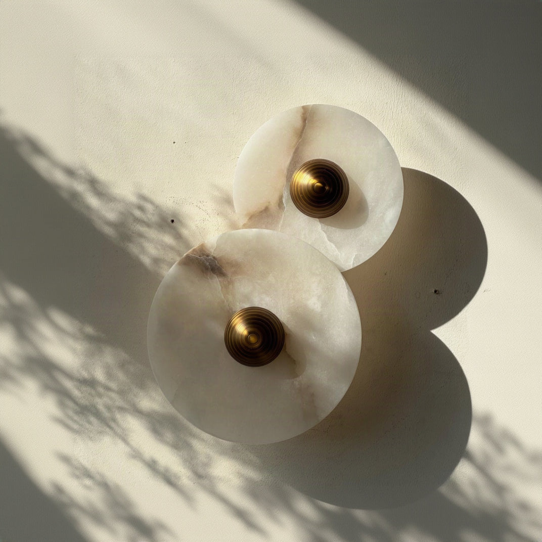 Two white Alabaster marble wall sconces with gold centers on a light background. IINK Interiors